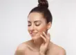 Woman with top bun closes her eyes and gently touches her cheek during a Sculptra treatment in Glendale, AZ; she has French-tipped nails.