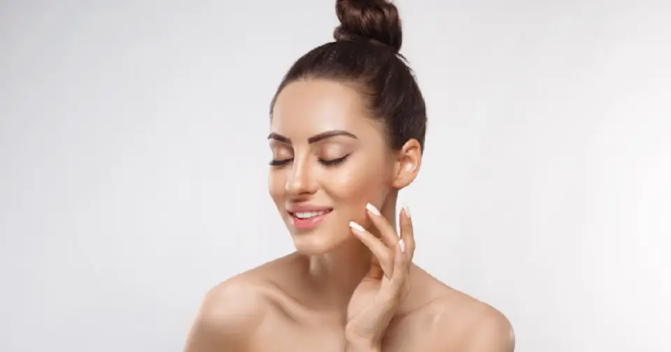 Woman with top bun closes her eyes and gently touches her cheek during a Sculptra treatment in Glendale, AZ; she has French-tipped nails.